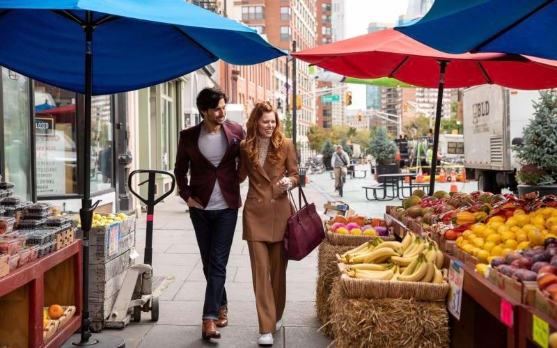 a man and a woman walking down a sidewalk next to a fruit stand